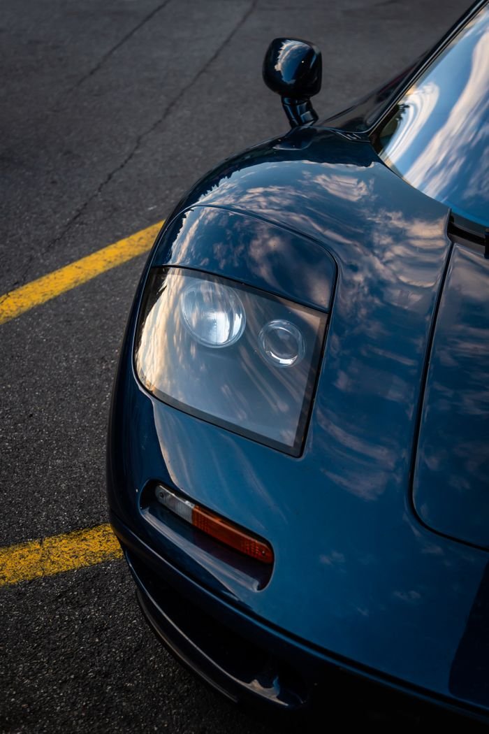 Front view of a luxury supercar with a reflective surface on an empty road at sunset.