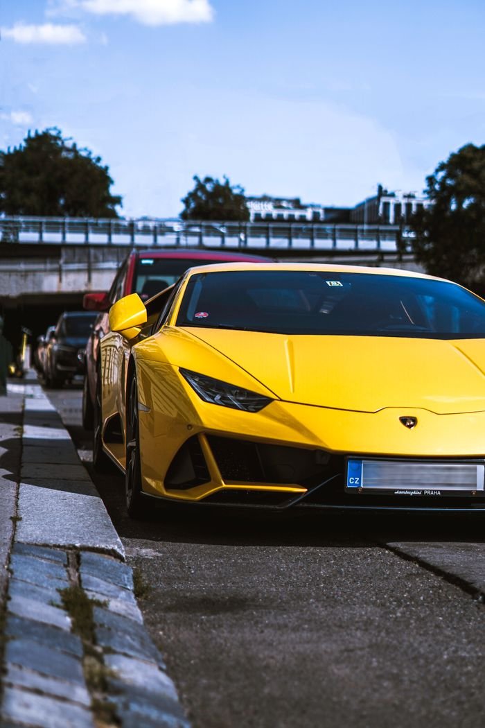 Services A vibrant yellow Lamborghini hypercar parked outdoors on a city road during the day.